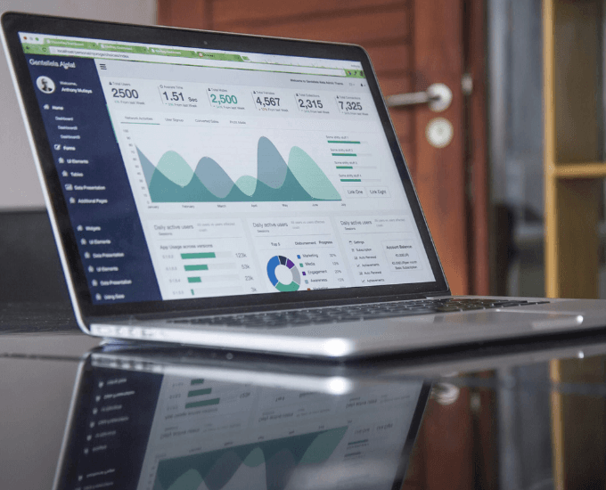 A laptop on a glass table showing an analytics dashboard with user counts, an area chart and a donut breakdown