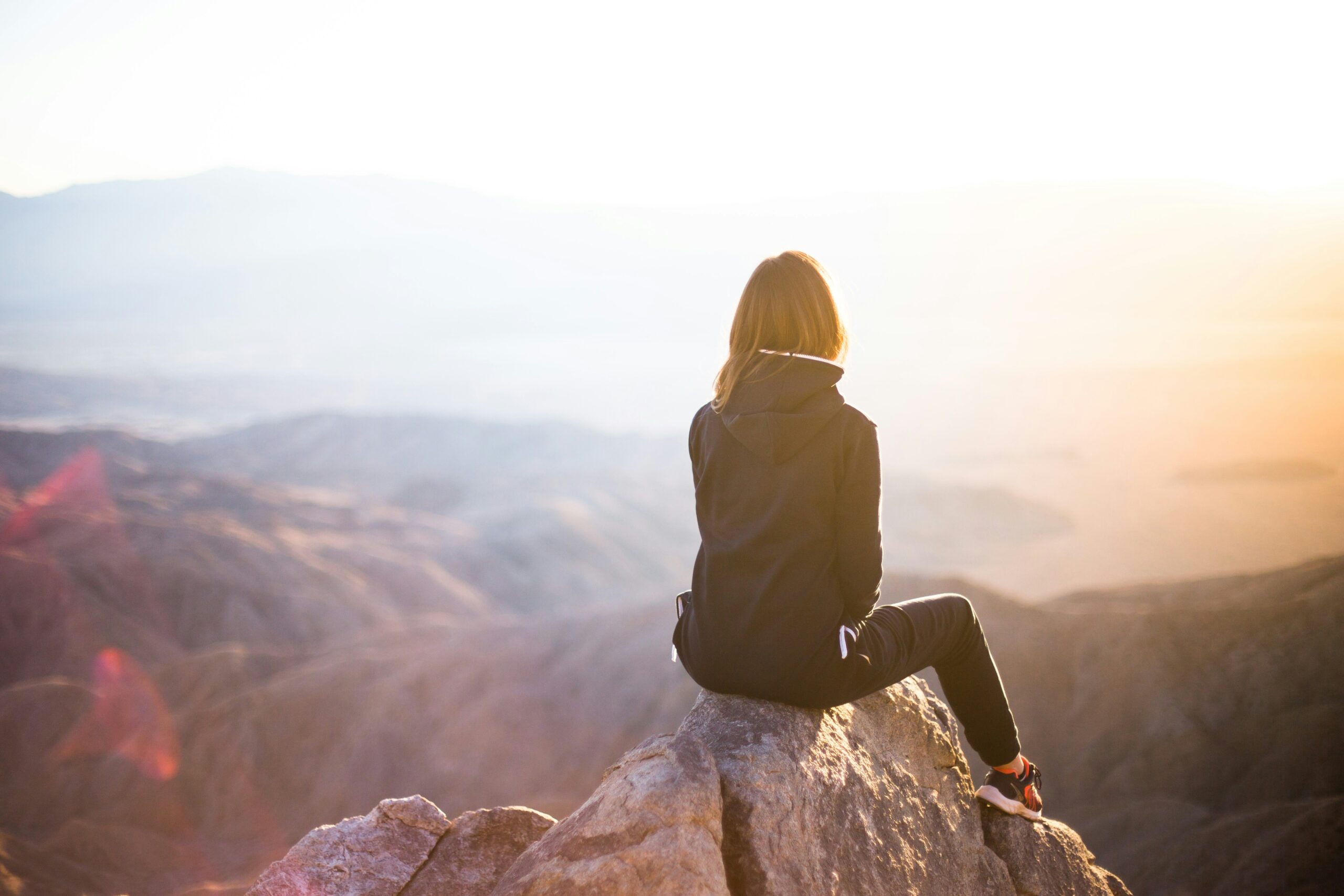 Person sitting on a rock overlooking a mountain valley at sunset